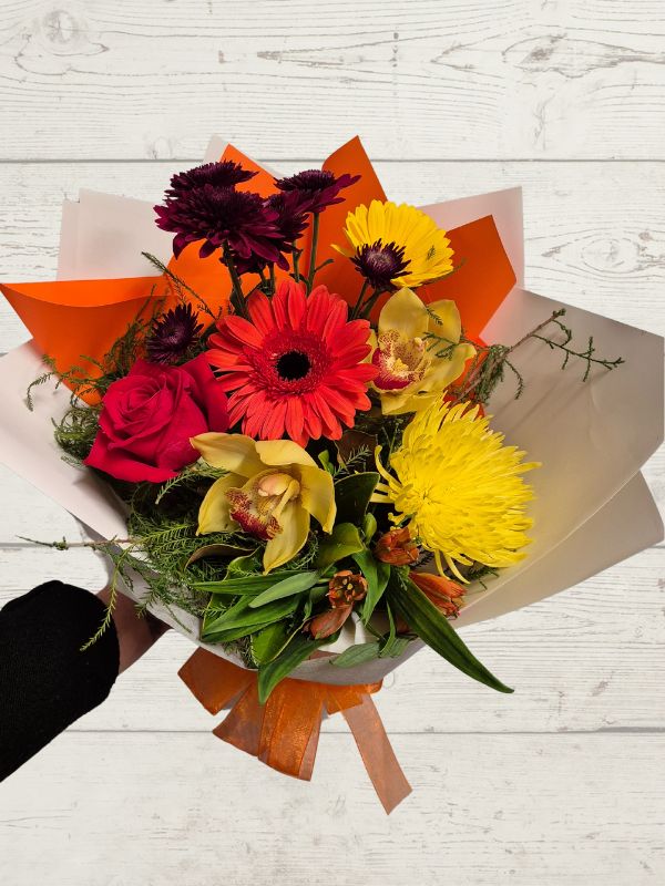 Colorful bouquet of flowers with orange and yellow accents on a light wooden surface