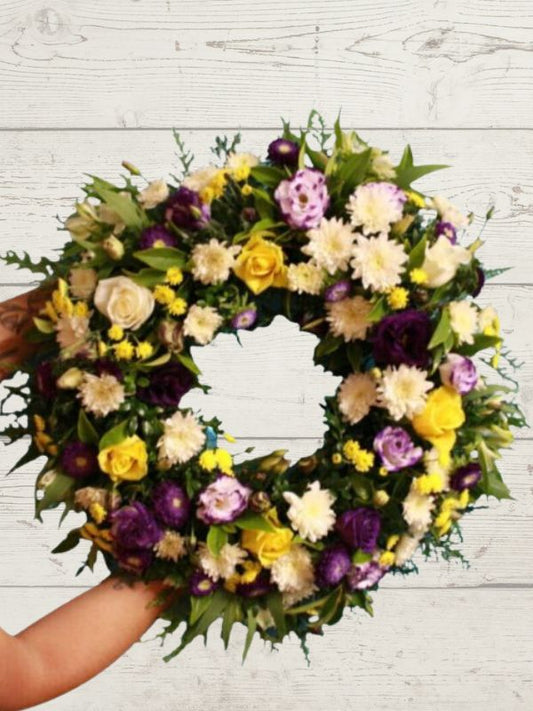 A Bright Sympathy wreath with a mix of purple, yellow, and white flowers, designed to be held in a hand.