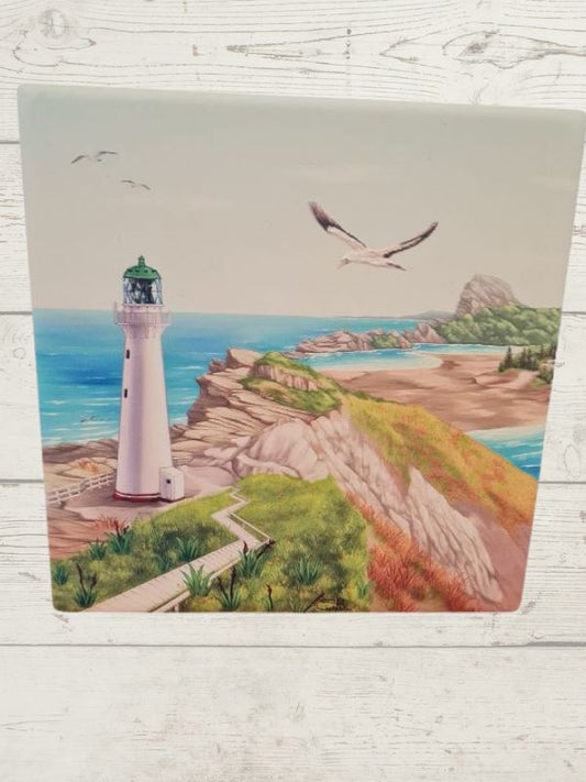 A ceramic tile featuring a lighthouse with a coastal and ocean background, with birds in flight.