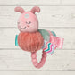 Pink plush toy with a teething ring on a wooden surface