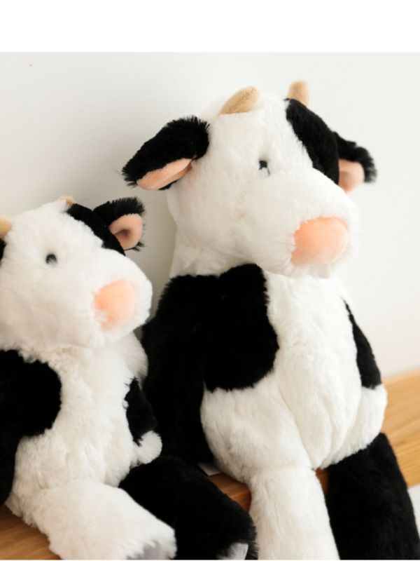 Two plush cow toys on a wooden surface with a white background