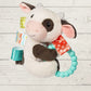 Plush toy cow with colorful tags and a teething ring on a wooden surface