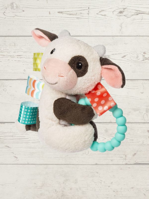 Plush toy cow with colorful tags and a teething ring on a wooden surface