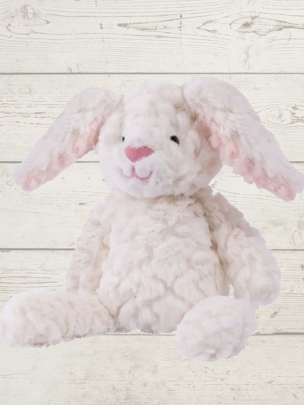 Two soft toy bunnies with beige and white coloring, sitting on a wooden surface. One bunny is plush and the other is a stuffed toy, both with embroidered eyes and a textured surface.