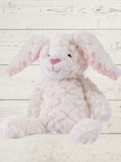 Two soft toy bunnies with beige and white coloring, sitting on a wooden surface. One bunny is plush and the other is a stuffed toy, both with embroidered eyes and a textured surface.