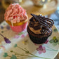 Two cupcakes on a plate, one with pink frosting and sprinkles, and the other with chocolate frosting and nuts.