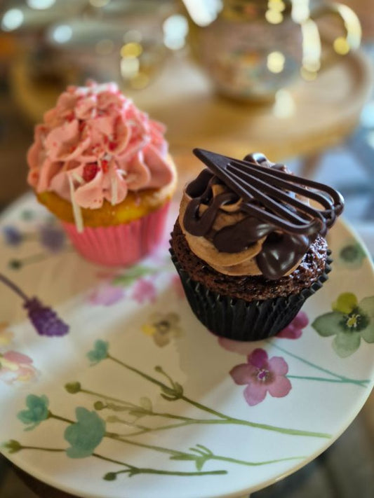 Two cupcakes on a plate, one with pink frosting and sprinkles, and the other with chocolate frosting and nuts.