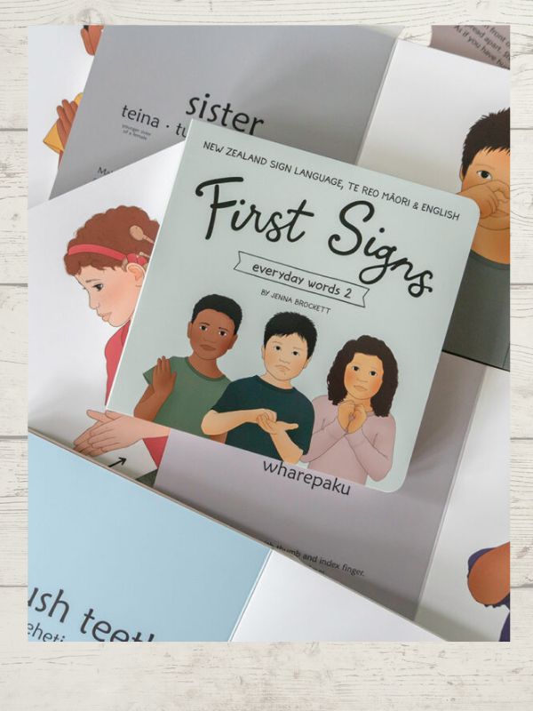 A book titled 'First Signs - Everyday words' with illustrations of adults and a child, showcasing New Zealand Sign Language.