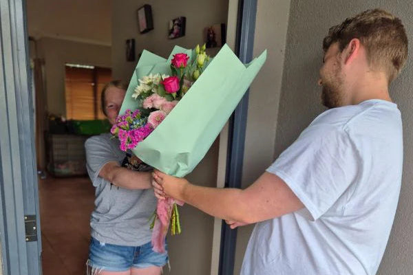 Person handing flowers to another person through a glass door.
