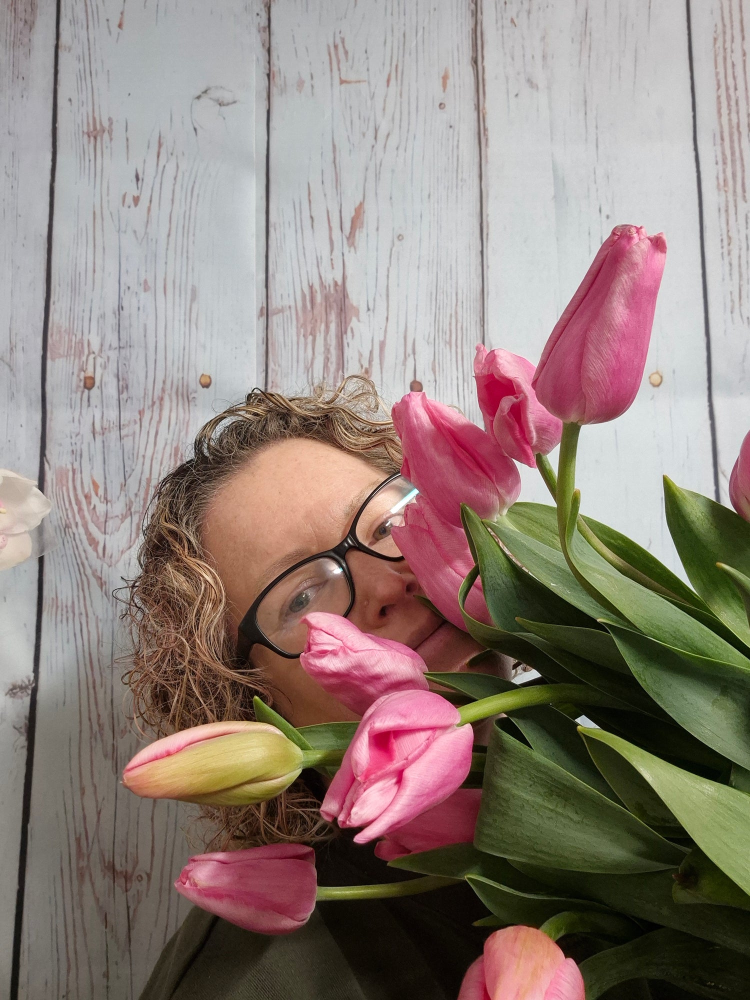 Person with glasses surrounded by pink tulips on a wooden surface
