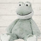A gray plush toy resembling a frog with embroidered details on the face and a soft body, placed against a wooden background.