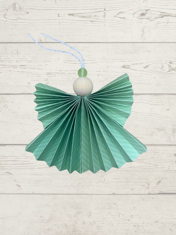 Green paper angel ornament on a light wooden background