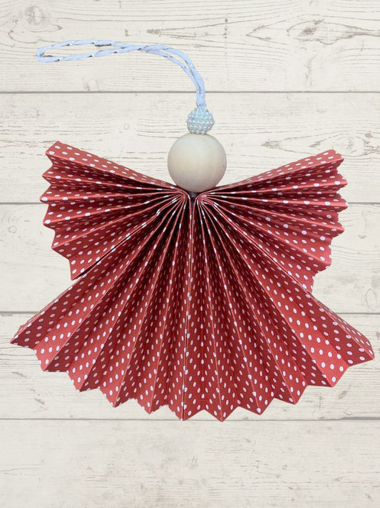 Decorative angel ornament with red polka dot wings and white ball on a light wooden background
