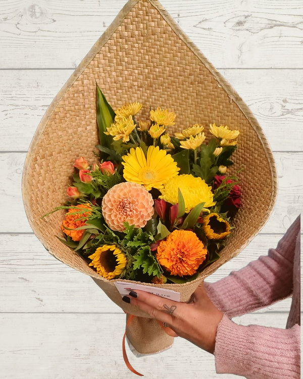 Bouquet of flowers wrapped in brown paper held by a person on a light wooden surface, Fresh flowers delivered in Hamilton