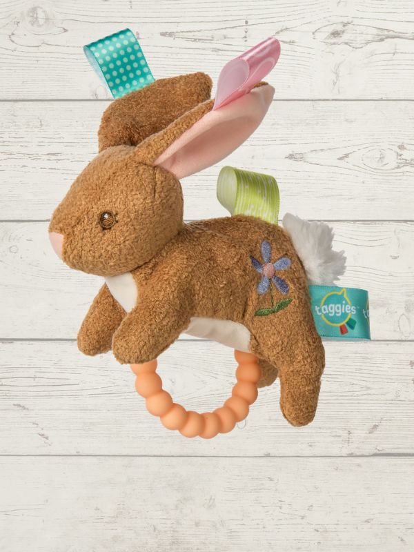 Plush bunny toy with teething ring and tags on a wooden surface