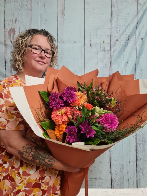 A person holding a hand-tied bouquet of hot pink and orange flowers, with seasonal variations in the flowers used.