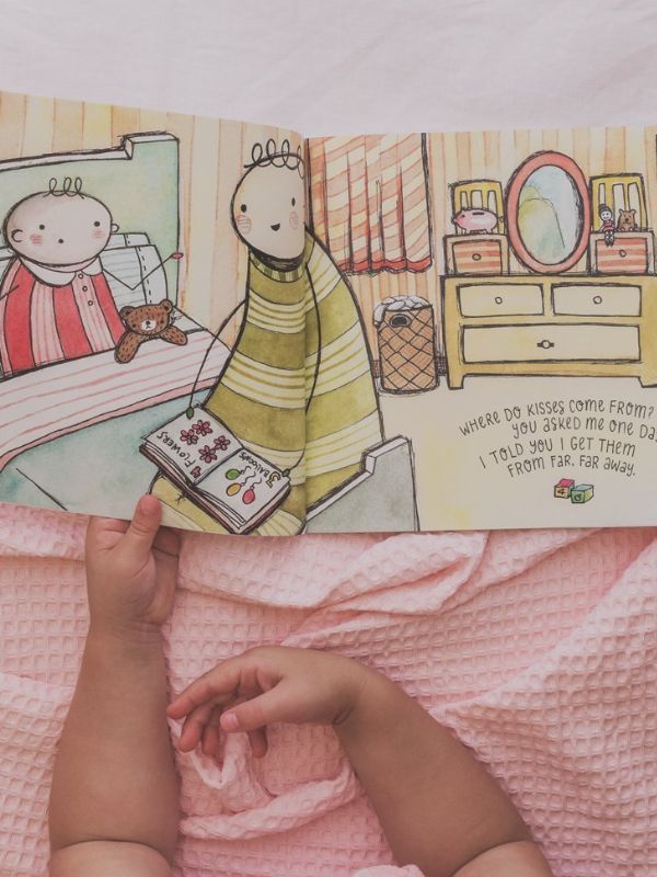 babys hands holding a paperback book with illustrations on it on a pink blanket