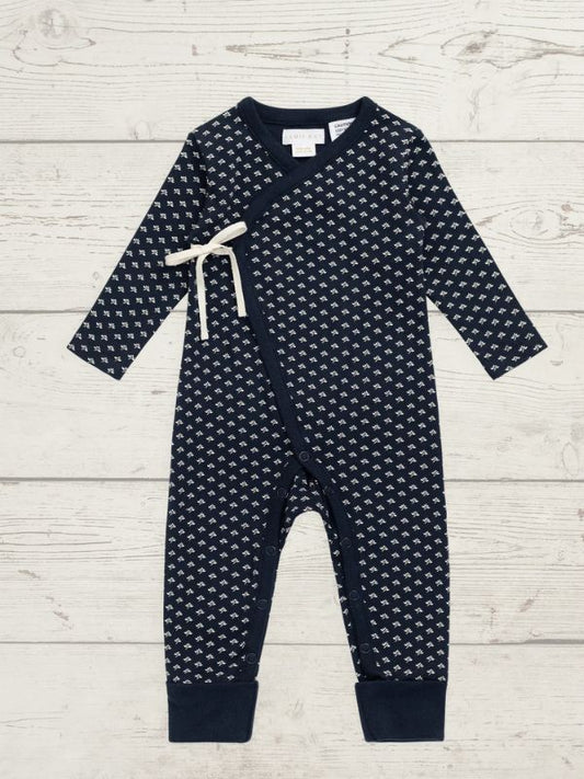 A baby long-sleeve footless romper in navy blue with a small white repeating pattern, featuring a cream-colored drawstring tie at the chest and ribbed cuffs at the ankles, laid flat on a light wood background.