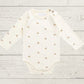 White baby bodysuit with gold patterns on a light wooden surface