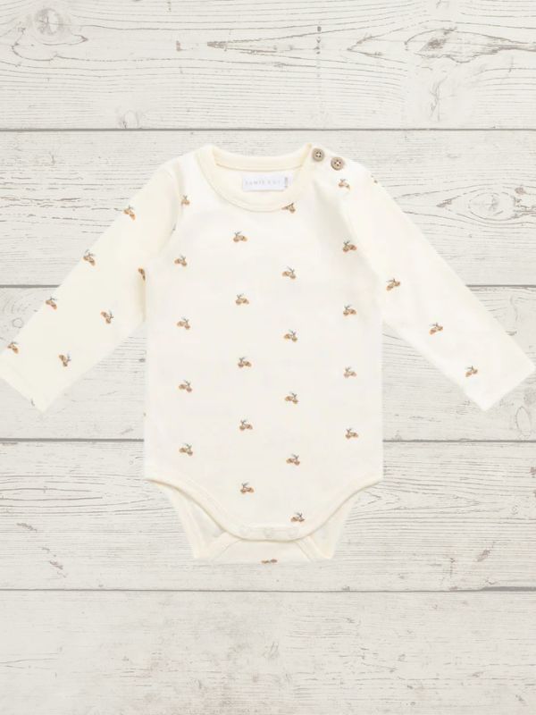 White baby bodysuit with gold patterns on a light wooden surface
