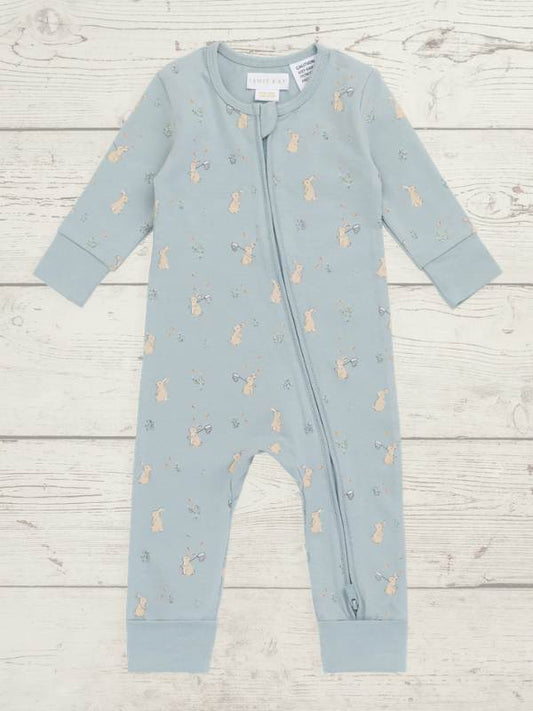 A baby's long-sleeve footless zip-up romper in dusty blue, featuring a repeating pattern of small beige bunnies, laid flat on a light wood plank background.