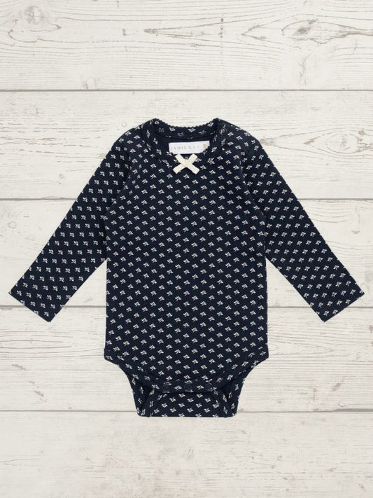 A baby long-sleeve bodysuit in navy blue with a small white geometric pattern, laid flat on a light gray wood plank background.