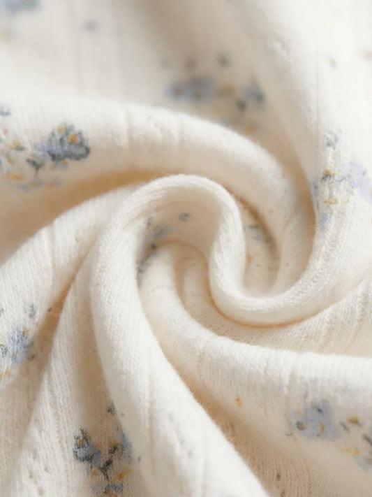 Close-up of a soft cream-colored cotton muslin fabric with a delicate blue and yellow floral pattern, styled in a spiral swirl.