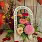 A colorful floral arrangement with a variety of flowers and greenery, displayed in a container with the text 'JUST FOR YOU' on it, against a wooden backdrop with heart decorations.
