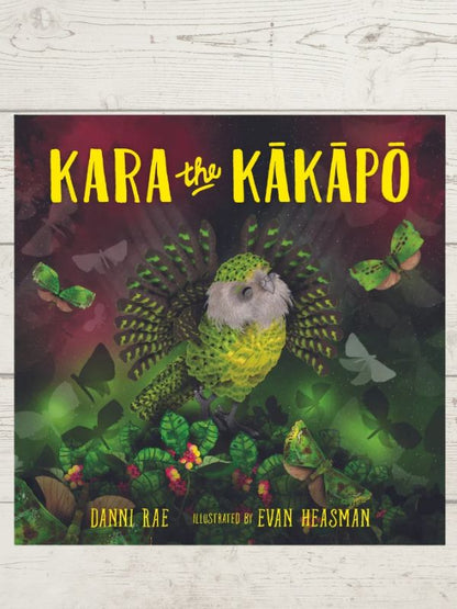 Children's book cover titled 'KARA the KÁKÁPÖ' featuring a colorful illustration of a green and yellow bird surrounded by butterflies and foliage, set against a white wood-textured background.