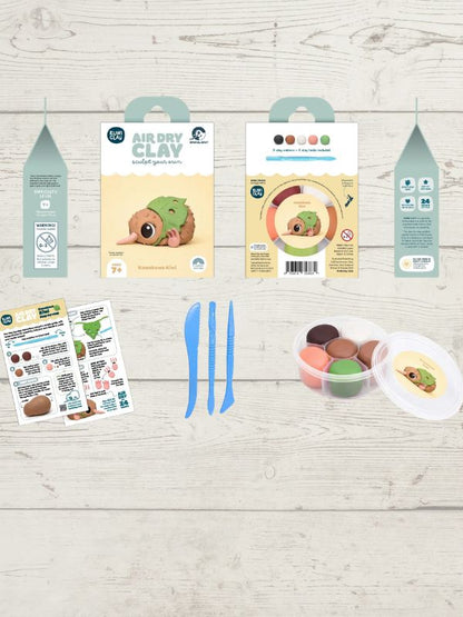 Air Dry Clay modeling kit components laid out on a light wood background, including three hanging packaging cards, two blue plastic tools, two instruction sheets, and a round plastic container with colorful clay balls and a small character-shaped piece.