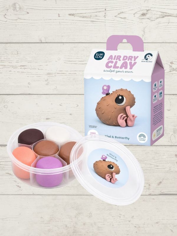 An air dry clay kit with a clear plastic container of colorful clay balls and its retail packaging box, displayed on a light wood background.