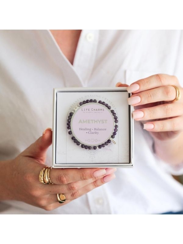 Person holding a box with a bracelet labeled 'Amethyst' against a white background