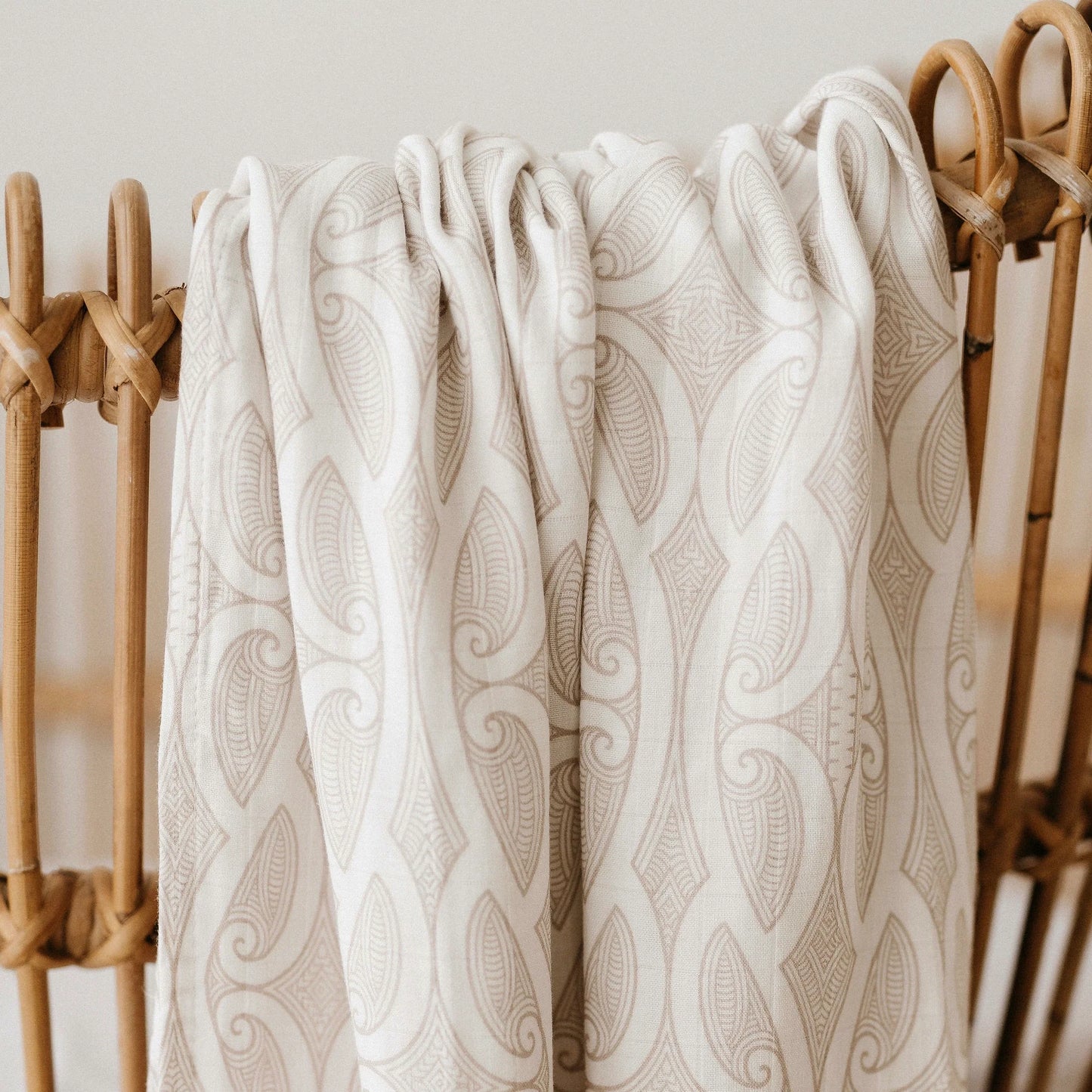 Patterned beige blanket draped over a wooden chair against a light background