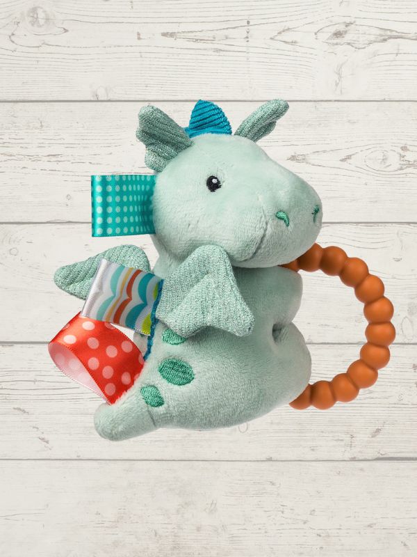 Plush dragon toy with a teething ring on a light wooden surface