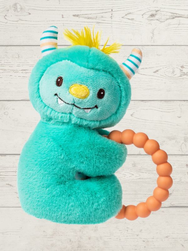 Teal plush toy with horns and a smile, holding an orange teething ring on a light wooden surface.