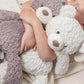 A child holding two plush bears, one in each arm, with a third bear beside them on the bed.