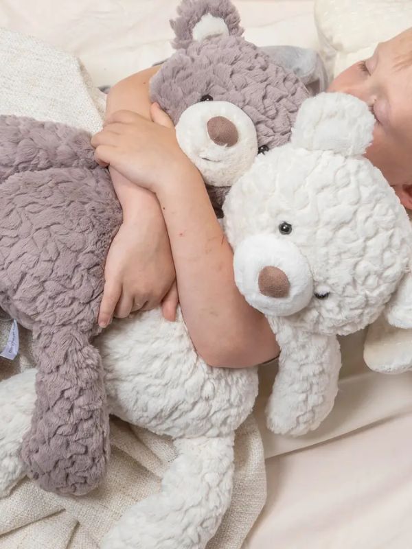 A child holding two plush bears, one in each arm, with a third bear beside them on the bed.