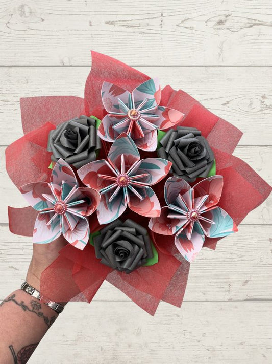 Bouquet of paper flowers with red, gray, and green colors on a wooden surface.