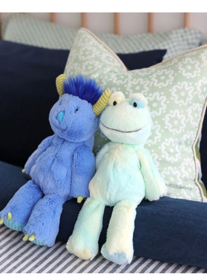 Two plush toys, one blue and one multicolored, sitting on a striped surface with pillows in the background.