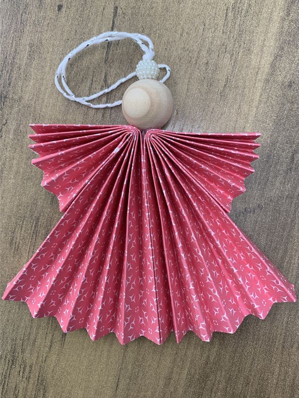 Decorative pink fan-shaped ornament with a wooden bead on a wooden surface