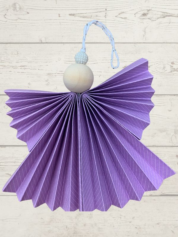 Purple angel-shaped decorative item with a white sphere and blue string on a light wooden background