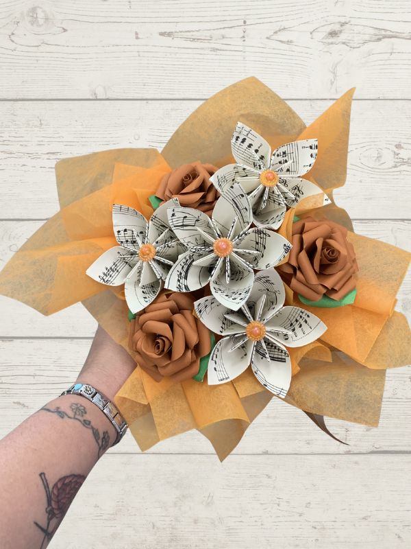 Bouquet with paper flowers and brown roses on a wooden surface