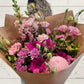 A bouquet of pastel-colored flowers including pink, white, and green, arranged in a paper-like bag.
