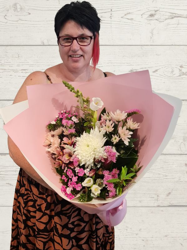 Person holding a pink and white bouquet with pink wrap. 