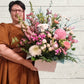 A person holding a pastel-colored floral arrangement with a variety of flowers in a box.