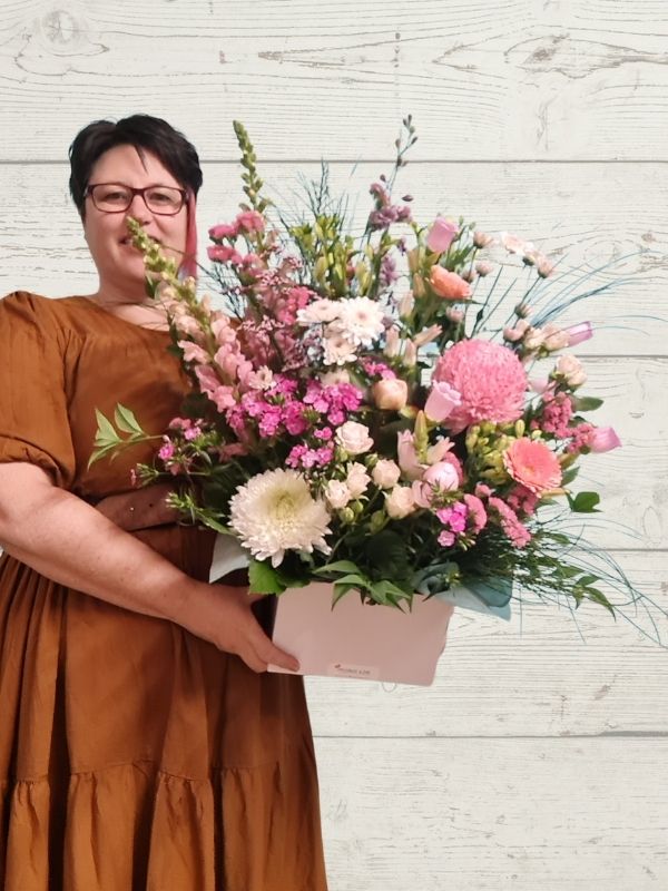 A person holding a pastel-colored floral arrangement with a variety of flowers in a box.
