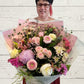 Person holding a large floral bouquet with flowers in pinks, white and mauve colours. Wrapped in white and pink. 