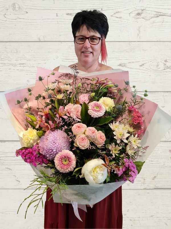 Person holding a large floral bouquet with flowers in pinks, white and mauve colours. Wrapped in white and pink. 