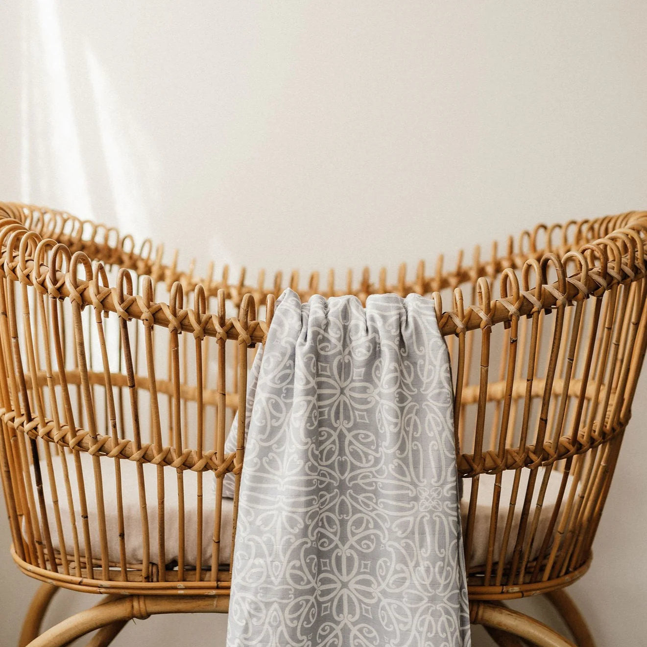 Wicker crib with a gray patterned blanket draped over it against a neutral background