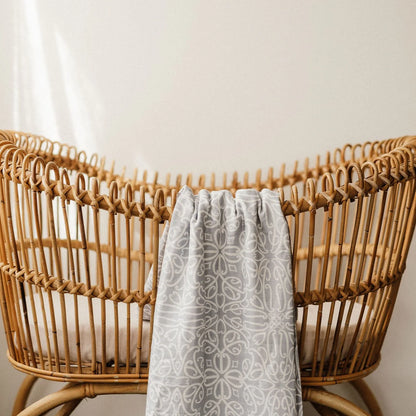 Wicker crib with a gray patterned blanket draped over it against a neutral background